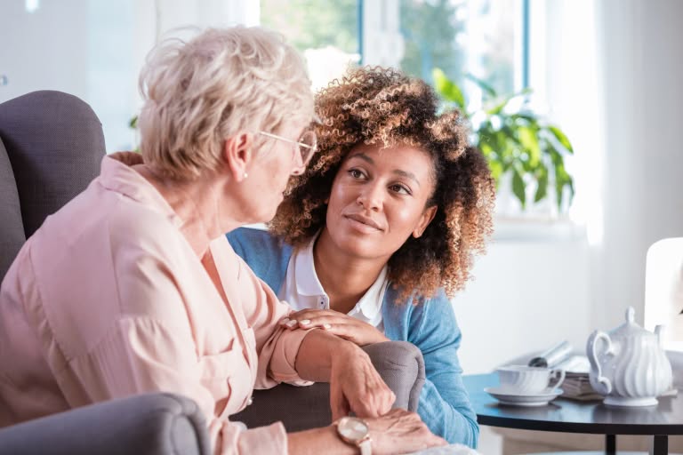 A caregiver sitting with an older woman and comforting her