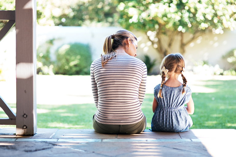 A mother and daughter sitting side by side on a back porch, talking